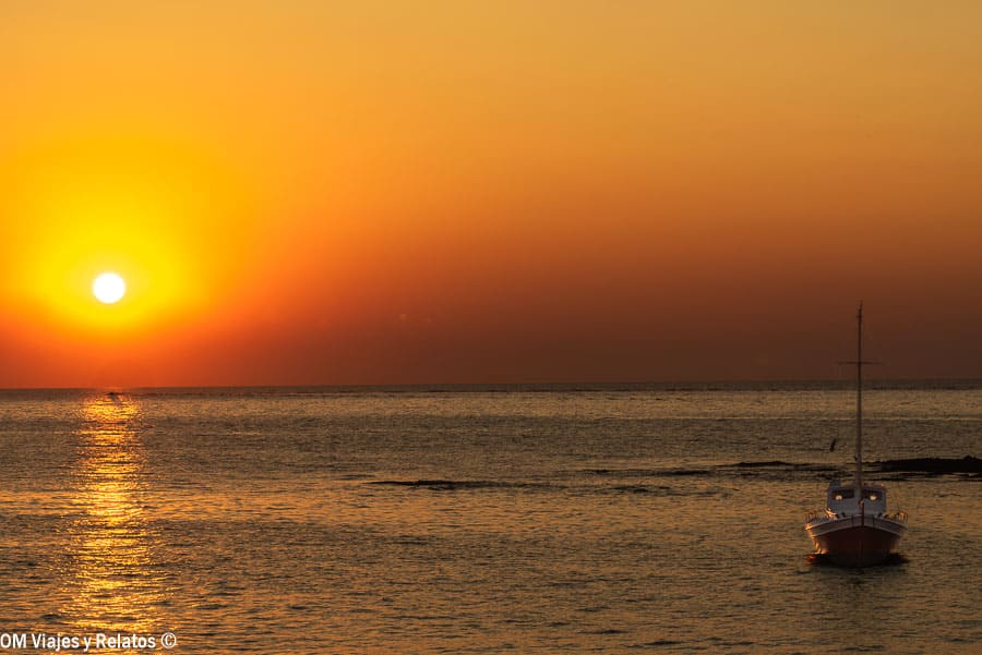 Atardecer frente al mar en Milos con un barco fondeado, una imagen inspiradora para planificar como llegar a Milos.