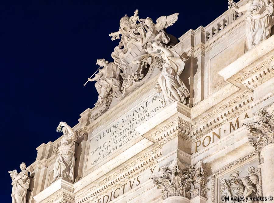 Detalle superior de la Fontana di Trevi con esculturas iluminadas de noche, información sobre la entrada a la Fontana di Trevi y acceso.