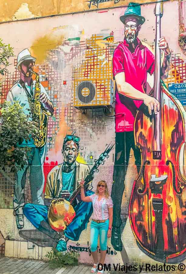 Servidora posando frente a un mural de arte callejero con músicos en Atenas, una zona alternativa y colorida que ver en Atenas en 2 días.