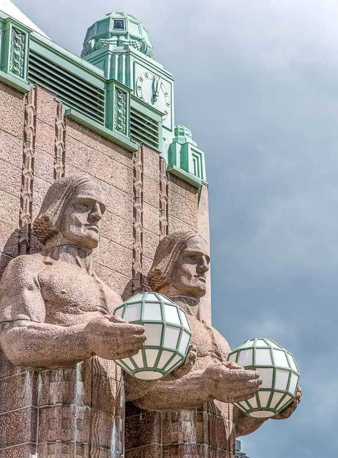 Figuras monumentales sosteniendo esferas luminosas en la estación central, símbolo art déco que ver en Helsinki en un día