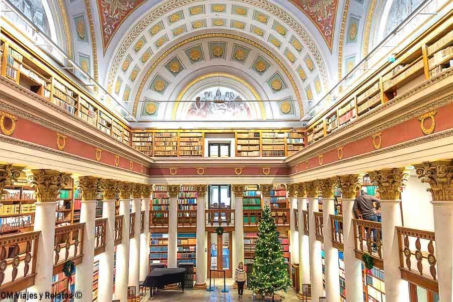 Salón principal de la Biblioteca Nacional con columnas y libros, una servidora en el centro, lugar histórico que ver en Helsinki en un día