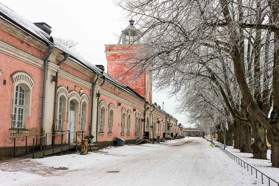 Calle nevada de Suomenlinna con casas rosadas históricas, paseo imprescindible que ver en Helsinki en un día