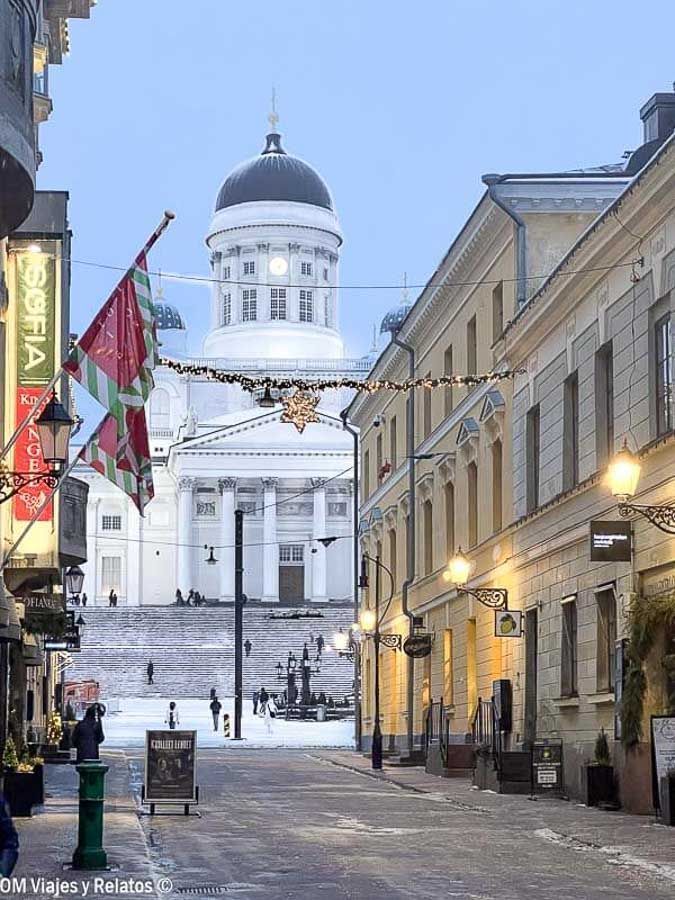 Vista de la escalinata nevada y la Catedral de Helsinki desde una calle comercial iluminada, uno de los rincones más bonitos que ver en Helsinki en un día