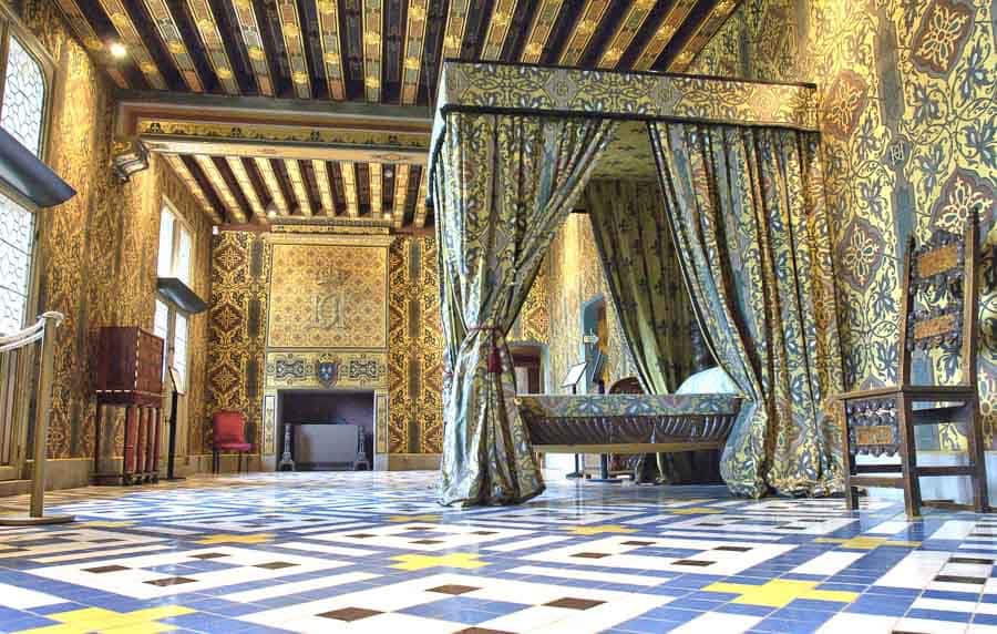 Dormitorio real del castillo de Blois decorado con ricos tapices dorados, mobiliario histórico y una impresionante cama con dosel, una visita imprescindible en una ruta por los castillos del Loira en coche.