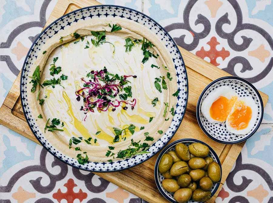Plato de hummus con aceite de oliva, perejil, cebolla morada, huevo cocido y aceitunas en restaurante de Budapest.
