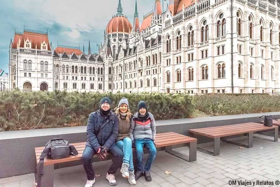 Foto familia posando en bancos frente al Parlamento de Budapest en invierno