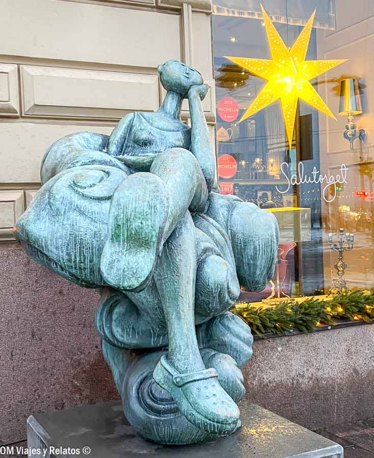 Escultura moderna de mujer pensativa frente a escaparate con estrella luminosa en Helsinki en Navidad