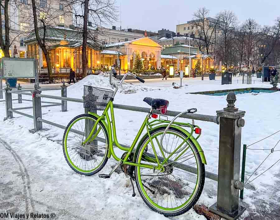 Parque cubierto de nieve con bicicleta y restaurante histórico decorado con luces en Helsinki en Navidad