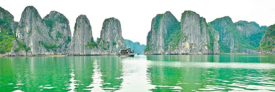 Barco en la bahía vietnamita rodeada de karsts y selva, visita que no puede faltar entre los imprescindibles de Vietnam.