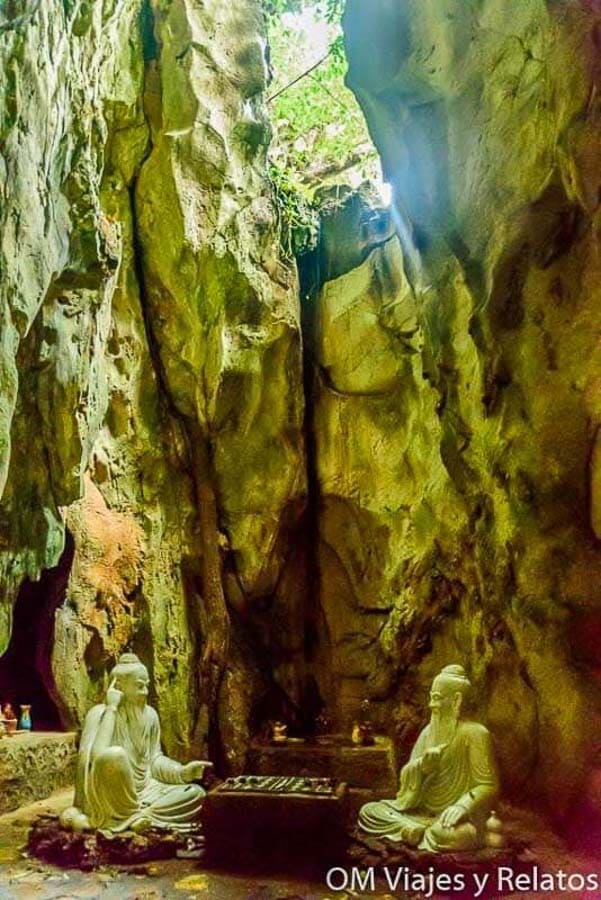Santuario budista dentro de una cueva en Vietnam, con estatuas blancas y luz natural entrando desde arriba.