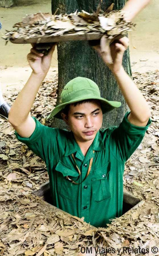 Guía vietnamita saliendo de un túnel de Cu Chi con la trampilla camuflada, visita histórica imprescindible en Vietnam.