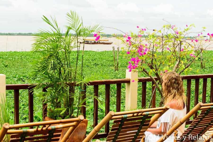 Relax en Vietnam: una servidora sentada frente a un paisaje fluvial verde con buganvilla rosa y embarcación tradicional.