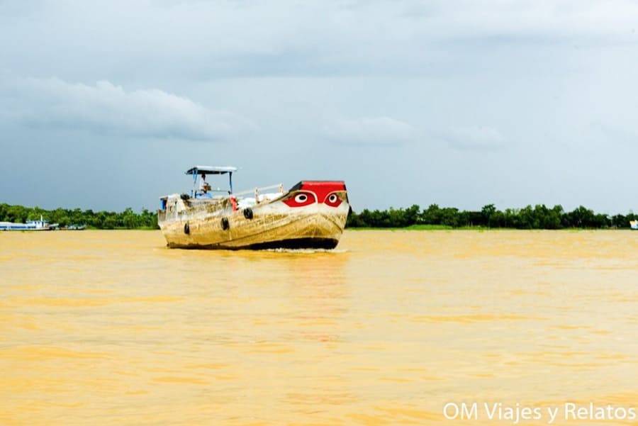 Barco tradicional navegando por el río Mekong en Vietnam, con proa pintada y paisaje selvático al fondo.