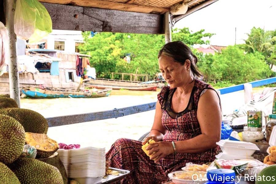 Mujer preparando fruta en un barco del delta del Mekong, escena gastronómica imprescindible en Vietnam.
