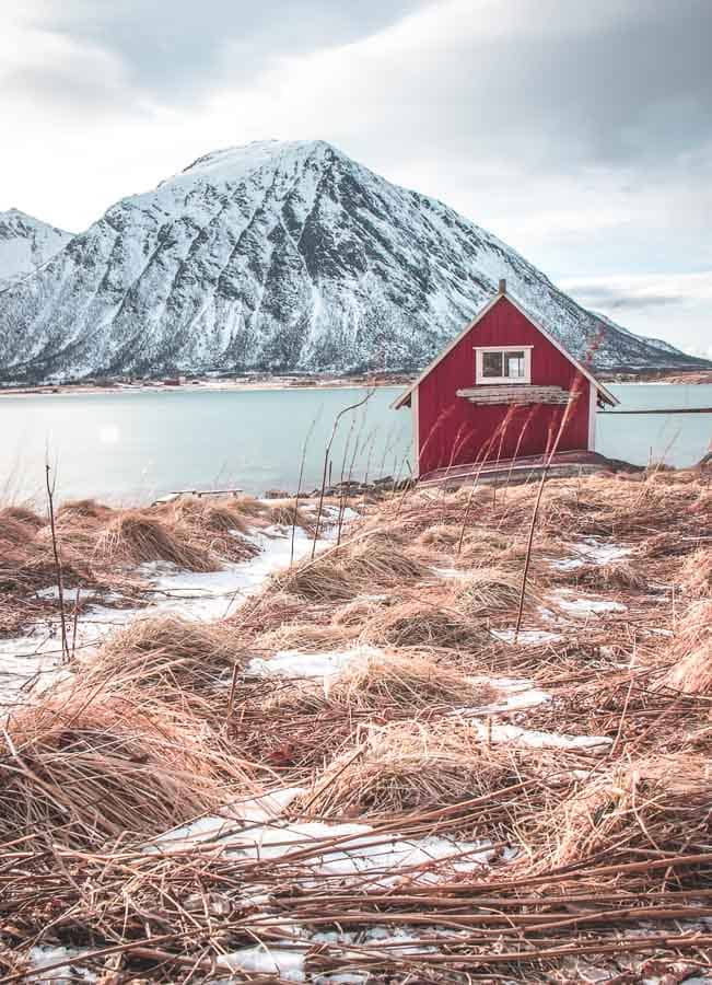 Pequeña cabaña roja junto al mar rodeada de montañas nevadas en Islandia en febrero