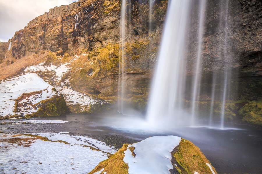 Cascada islandesa cayendo entre acantilados con nieve y hielo en Islandia en febrero