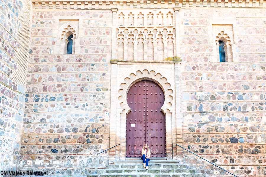 Fachada mudéjar de Toledo con gran puerta medieval y una servidora sentada en las escaleras, que ver en Toledo en un día