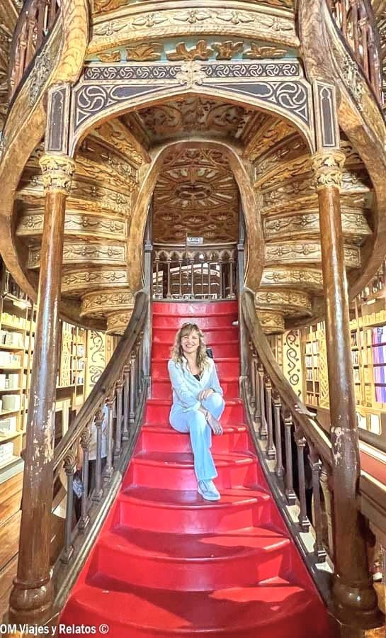 Servidora posando en la icónica escalera roja de la Librería Lello en Oporto, una visita imprescindible que ver en Oporto en 2 días.