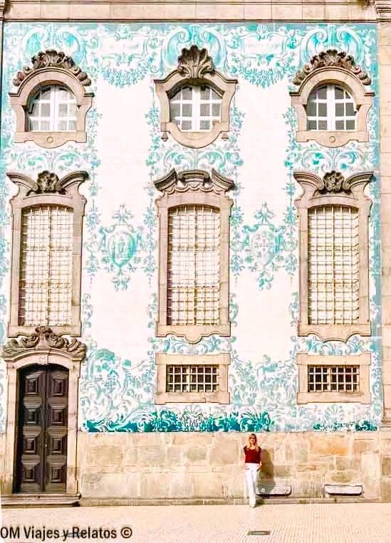 Fachada con azulejos azules y blancos de una iglesia barroca en el centro histórico de Oporto, con una mujer posando al pie del edificio, uno de los lugares imprescindibles que ver en Oporto en 2 días.