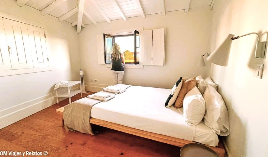 Habitación minimalista de hotel en Oporto, con cama doble y una mujer mirando por la ventana al atardecer, alojamiento con encanto donde dormir mientras descubres qué ver en Oporto en 2 días.