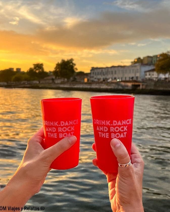 JC y yo brindando con vasos rojos en un paseo en barco por el río Duero al atardecer, una experiencia imprescindible que ver en Oporto en 2 días.