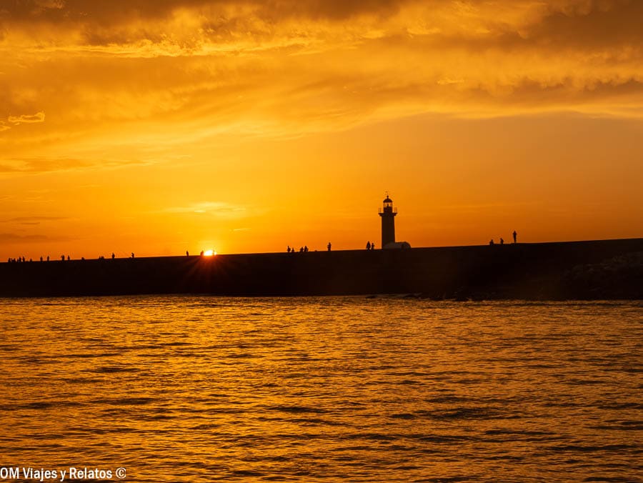 Atardecer dorado en la Foz do Douro con el faro en silueta y gente paseando por el espigón, una puesta de sol imprescindible que ver en Oporto en 2 días.