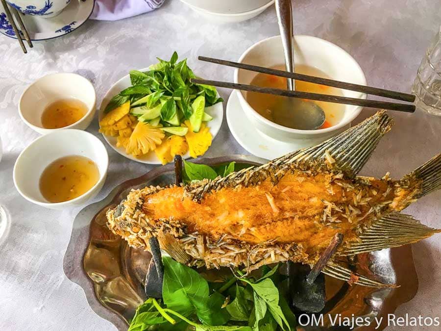 Delta del Mekong Vietnam: pescado frito entero con hierbas frescas, piña y salsas tradicionales servido en mesa.