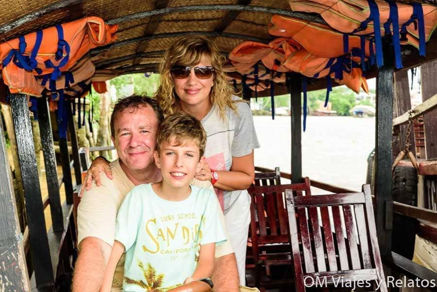 Foto familiar de OM Viajes y Relatos posando en una embarcación tradicional durante un paseo en barco por el delta del Mekong, Vietnam.