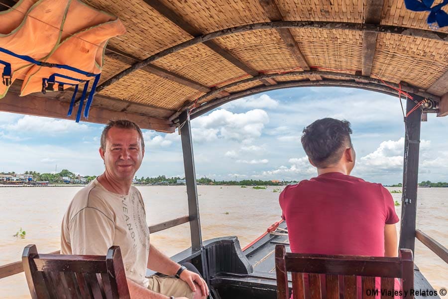 Delta del Mekong Vietnam: paseo en barco por el río con JC a bordo y paisaje fluvial en día nublado.