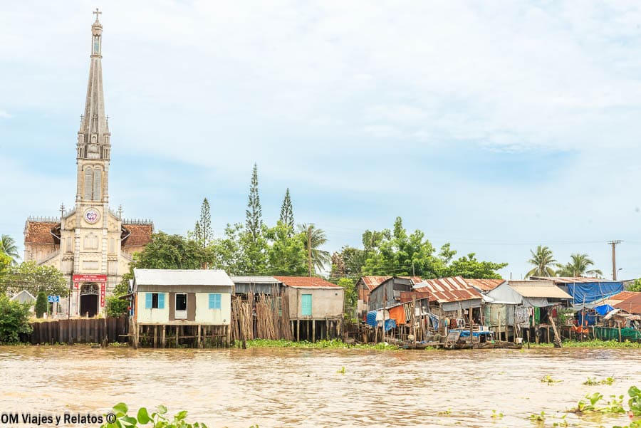 Delta del Mekong Vietnam: iglesia junto al río con casas tradicionales sobre pilotes en la orilla.