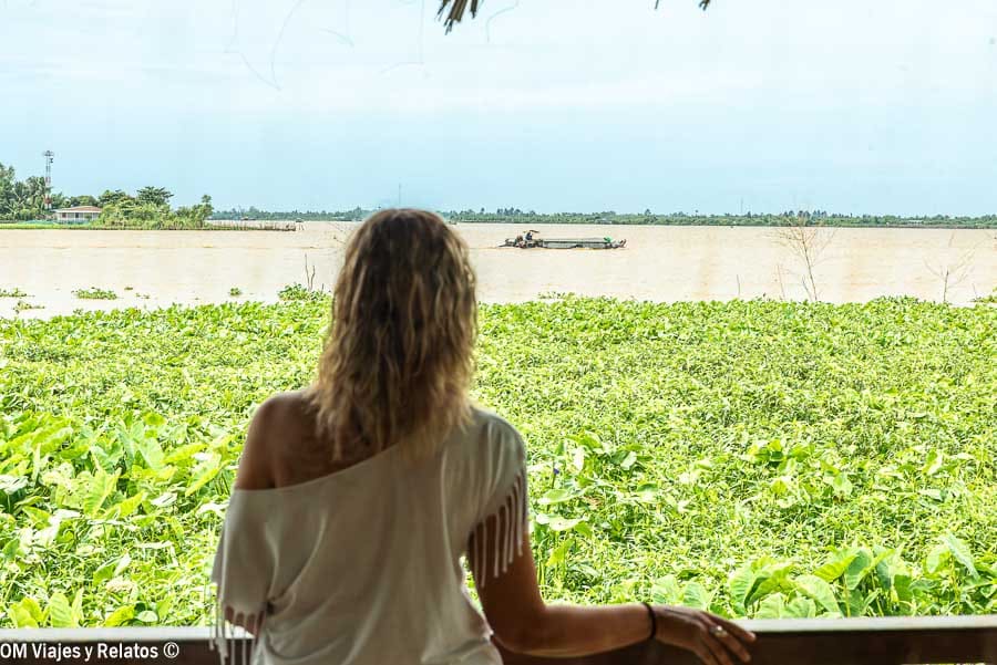 Una servidora de espaldas en la terraza del Mekong Riverside Resort, contemplando el río del Delta del Mekong con vegetación flotante y barcas al fondo, Vietnam