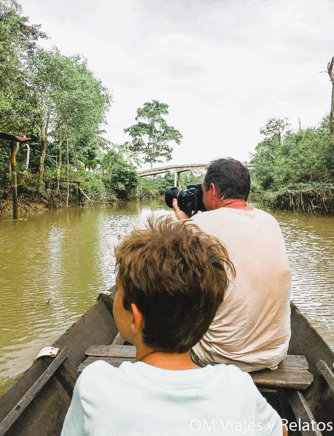 Delta del Mekong Vietnam: paseo en barca por un canal entre manglares, con JC fotografiando y nuestro hijo Raúl sentado en la proa.