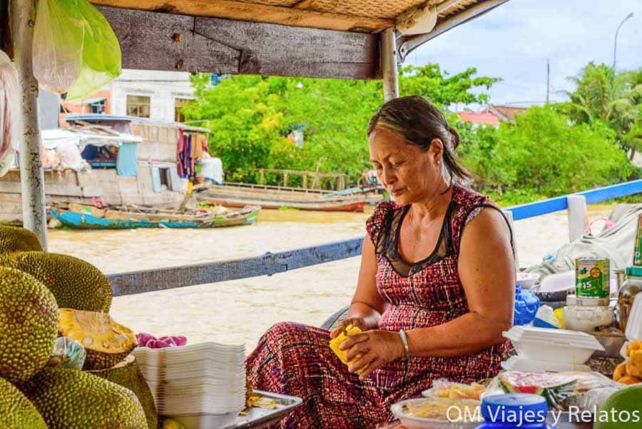 Delta del Mekong Vietnam: vendedora en mercado flotante preparando fruta tropical en una barca junto al río.