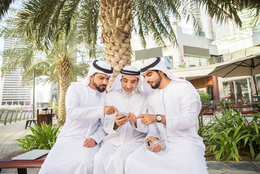 Tres hombres emiratíes usando un smartphone en Dubái, ejemplo cotidiano de como tener internet en Dubai en cualquier lugar.