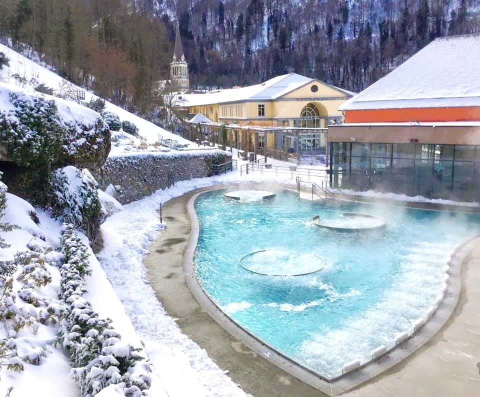 Piscina termal exterior de Les Bains du Rocher con vapor y nieve alrededor, un plan de relax en la ruta por los pueblos más bonitos del Pirineo Francés.