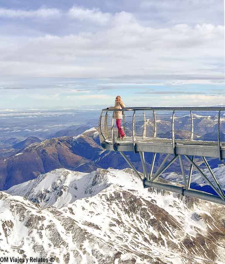 Una servidora en el mirador de Pic du Midi (pontón del cielo) sobre una pasarela suspendida con vistas a cumbres nevadas, una experiencia cerca de los pueblos más bonitos del Pirineo Francés.