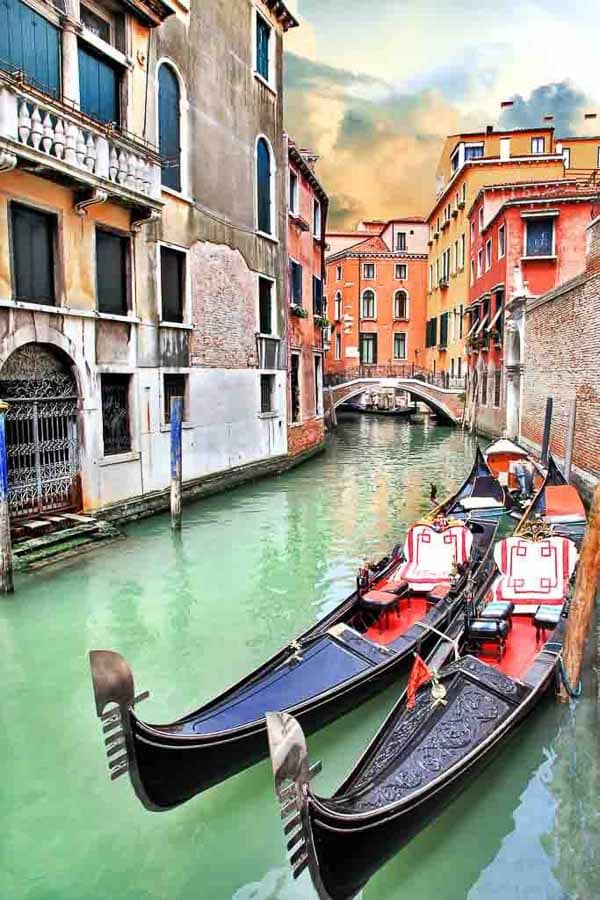 Góndolas en un canal estrecho de Venecia con casas de colores y un puente al fondo, qué ver en Venecia en 3 días.