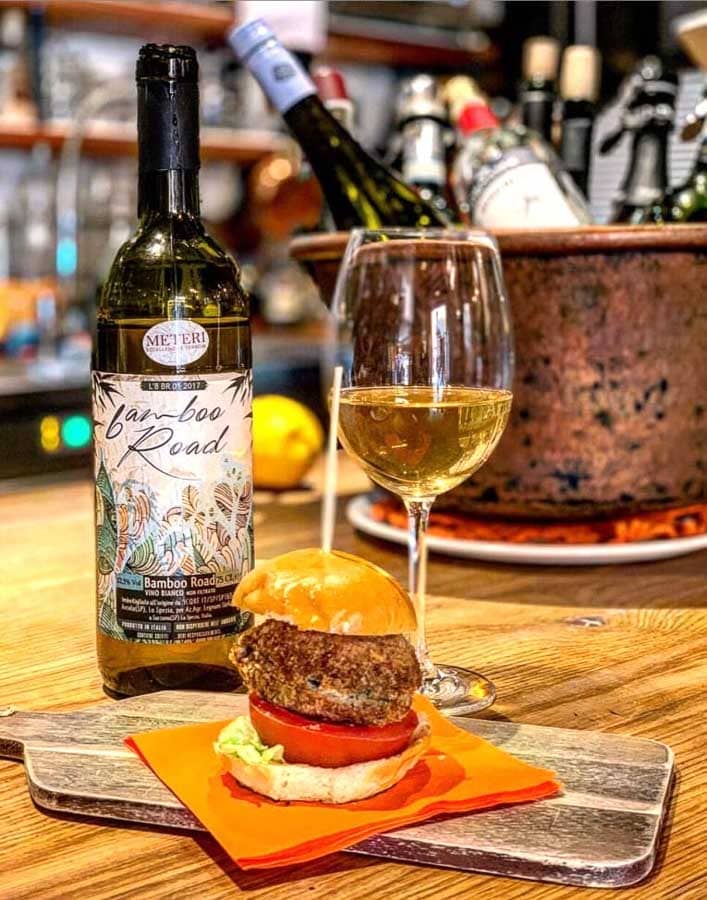 Que ver en Venecia en 3 días: aperitivo en Cantina Arnaldi con copa de vino blanco, botella y mini hamburguesa sobre la barra.