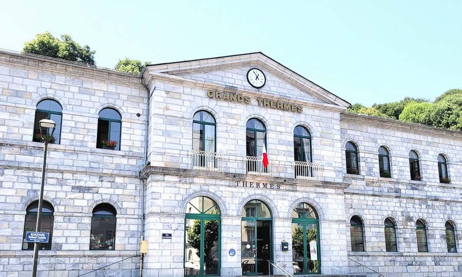 Fachada del balneario Les Grands Thermes de Bagnères-de-Bigorre con reloj y edificio de piedra, una parada de relax en la ruta por los pueblos más bonitos del Pirineo Francés.