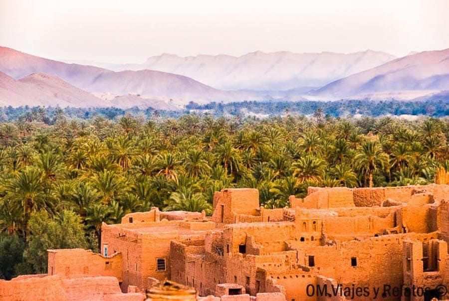 Kasbah de adobe junto a un palmeral y montañas del Atlas, ideal para consejos para viajar a Marruecos por el sur.
