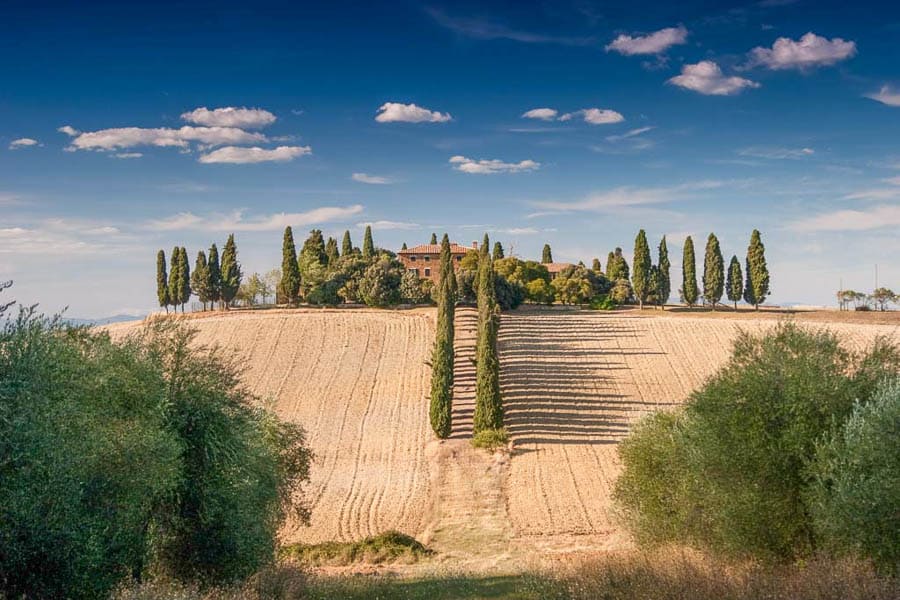Paisaje típico de la Toscana con cipreses y una casa rural en lo alto, una de las excursiones desde Roma de un día más bonitas.