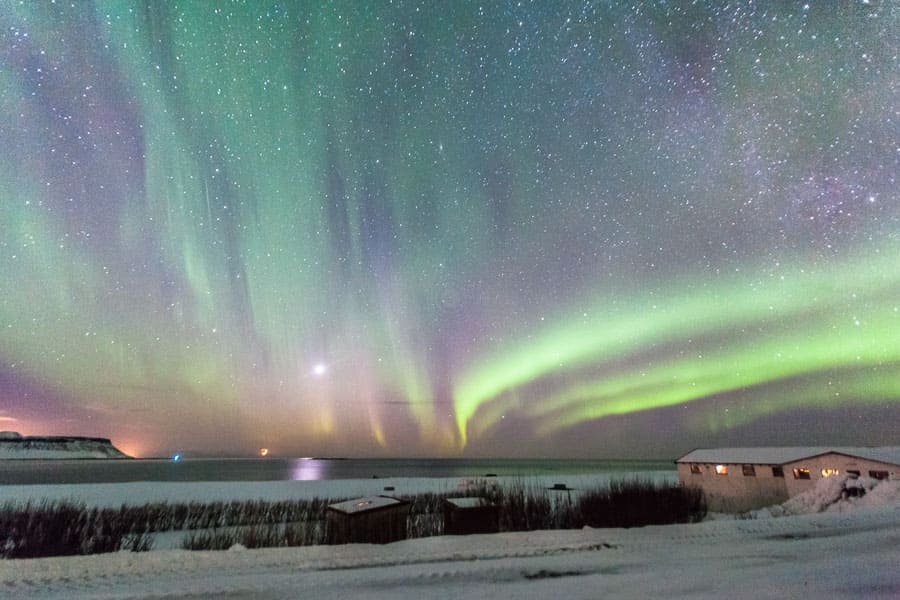 Aurora boreal sobre un paisaje nevado con casas y cielo estrellado, una noche mágica en Islandia en octubre.