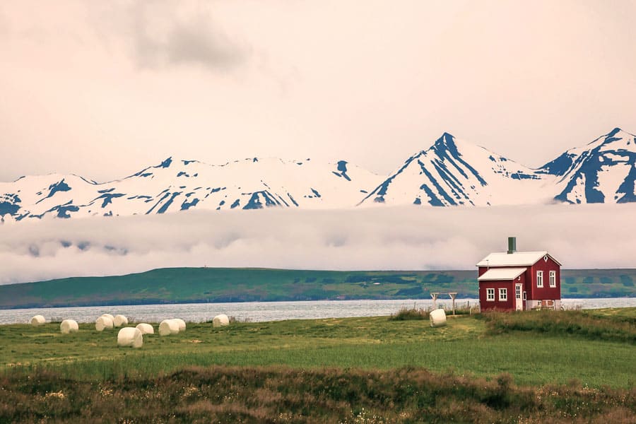 Casa roja junto al agua con montañas nevadas al fondo, un paisaje precioso de Islandia en octubre.