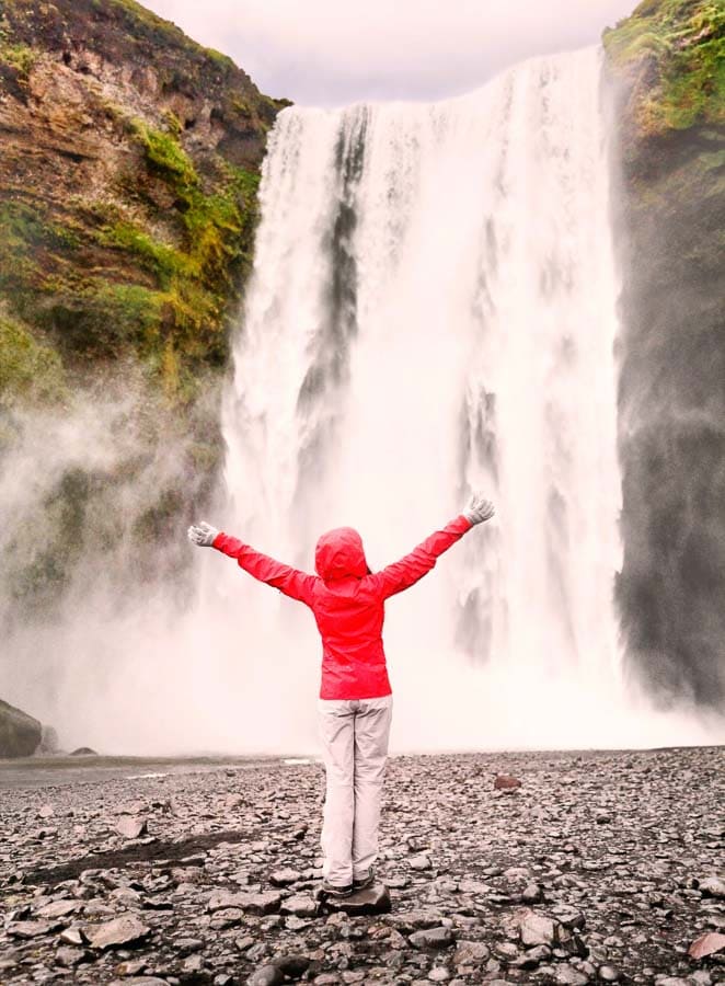 Servidora con chaqueta roja frente a una gran cascada en Islandia, una parada imprescindible en Islandia en octubre