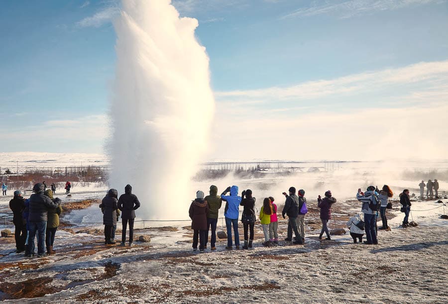 Géiser en erupción con visitantes alrededor, una de las paradas imprescindibles en Islandia en octubre.