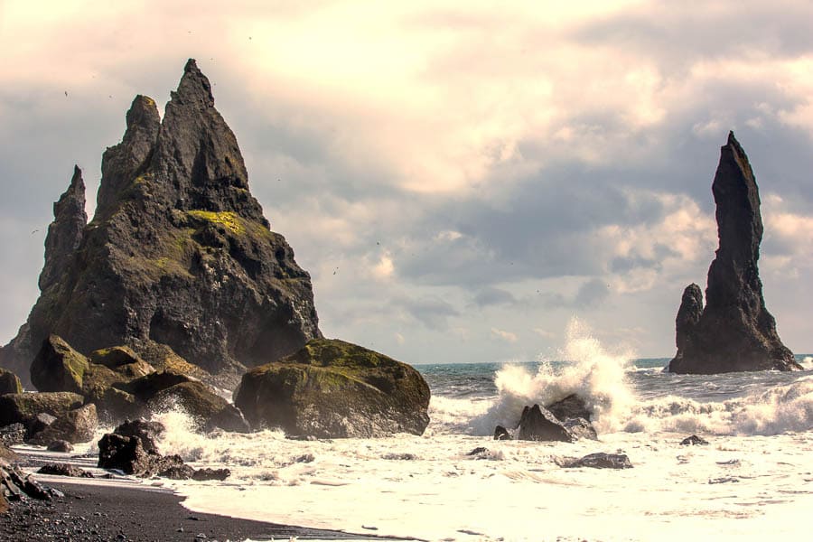 Farallones en el mar y olas en una playa de arena negra, un paisaje brutal de Islandia en octubre.