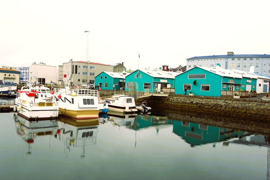 Puerto con barcos y casas de colores reflejadas en el agua, una escena típica de Islandia en octubre.