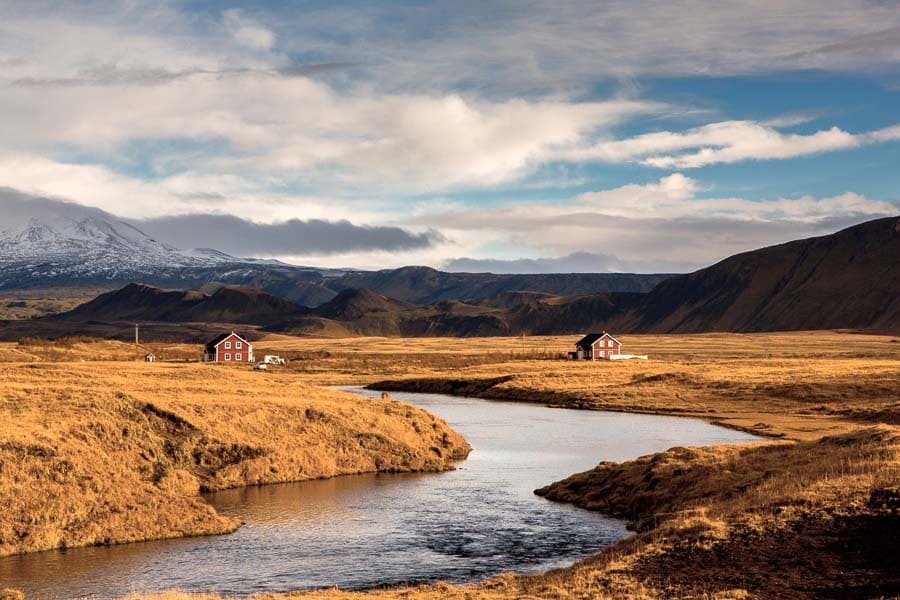 Río entre praderas doradas con casas rojas y montañas al fondo, un paisaje típico de Islandia en octubre.