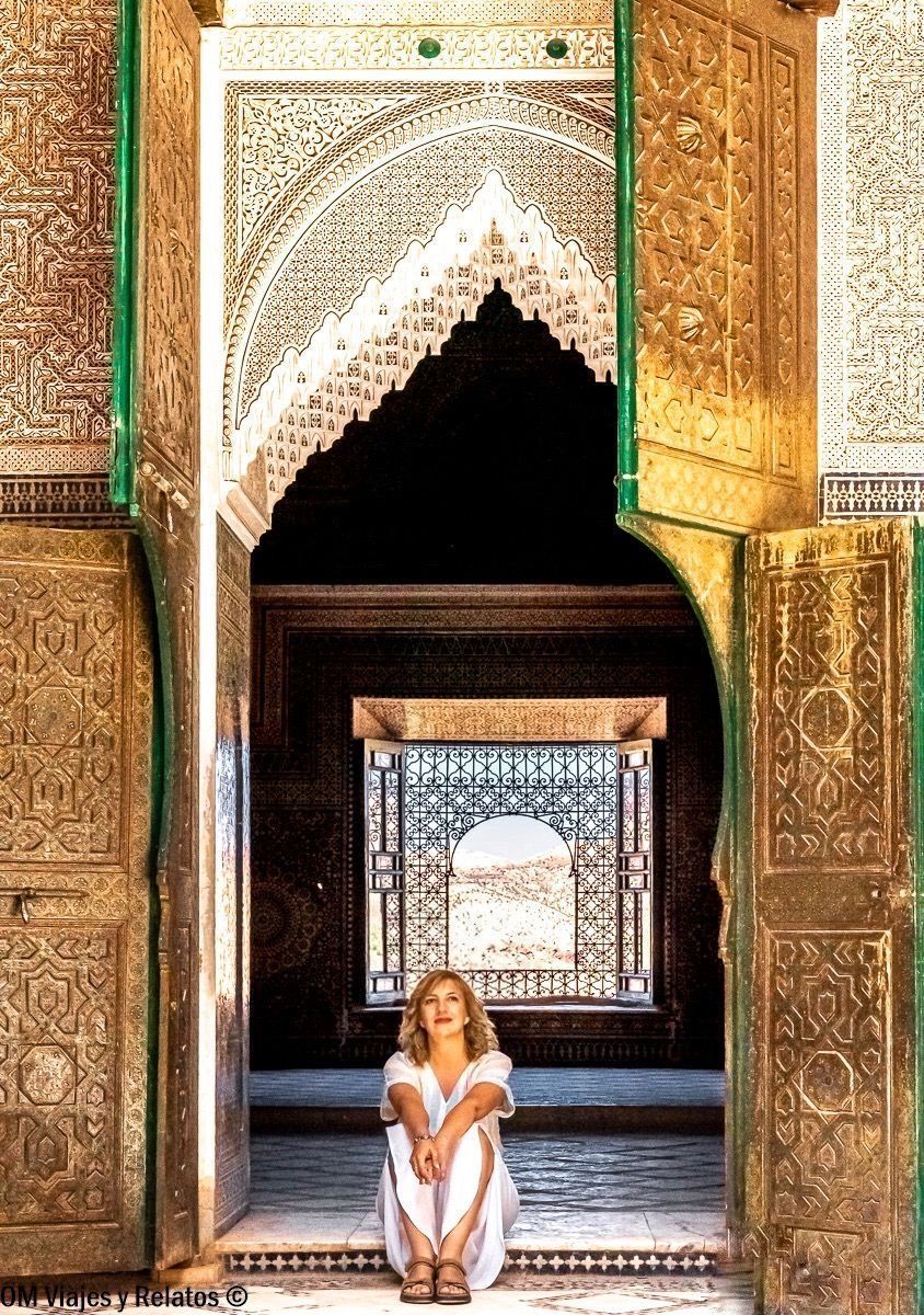 Servidora sentada en una puerta con arcos y azulejos marroquíes en una medersa, parada fotogénica en una ruta por Marruecos en coche.