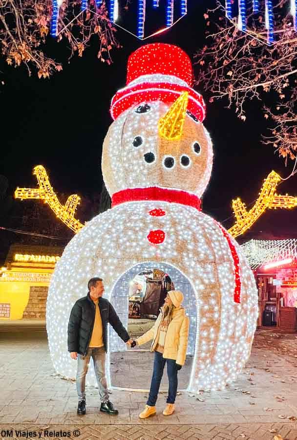 Pareja OM Viajes y Relatos posando frente a muñeco de nieve gigante iluminado en Madrid, plan divertido que hacer en Madrid en Navidad gratis.